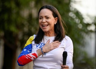 🕊️ María Corina Machado gana el Premio Nobel de la Paz 2025 por su lucha democrática en Venezuela María Corina Machado con micrófono en acto público vestida con camiseta tricolor de Venezuela